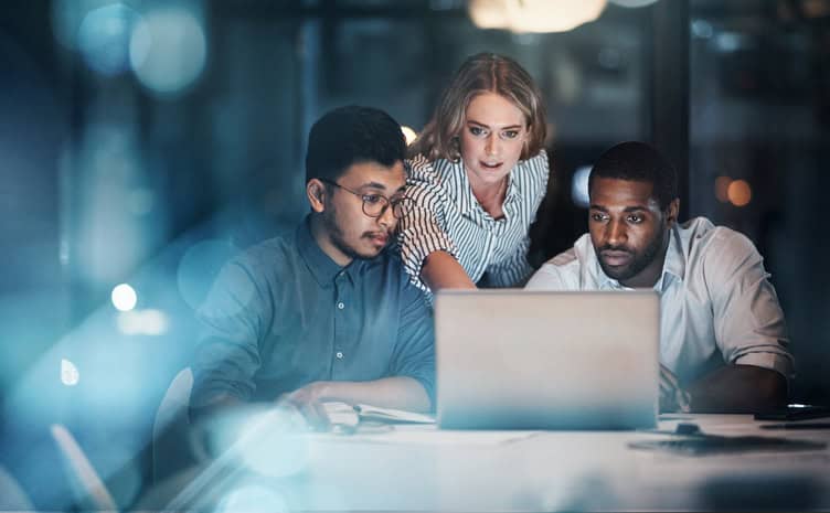 Cropped shot of three young business people working together on a laptop in their office late at night